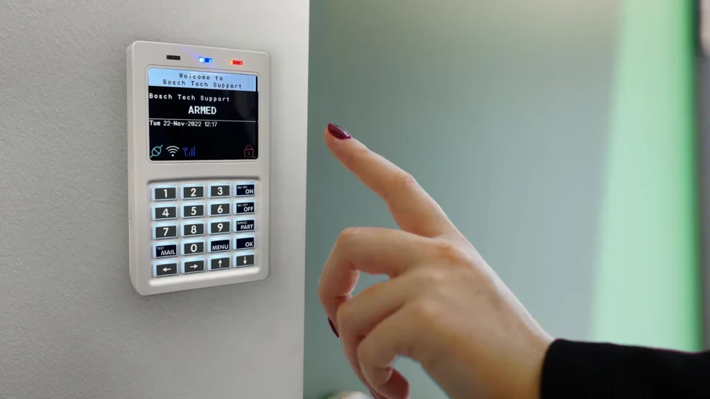 A wall-mounted alarm keypad showing an armed system, with a hand reaching to disarm it
