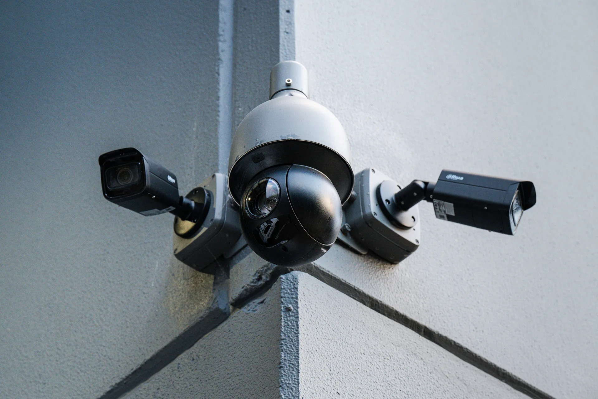 A pan-tilt-zoom dome camera flanked by two bullet cameras on a building corner