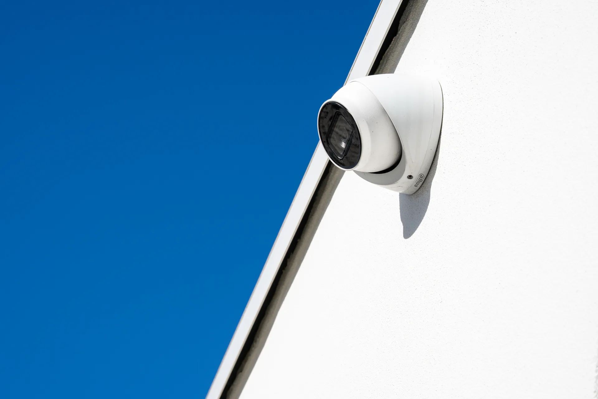 A white turret camera mounted against a clear blue sky