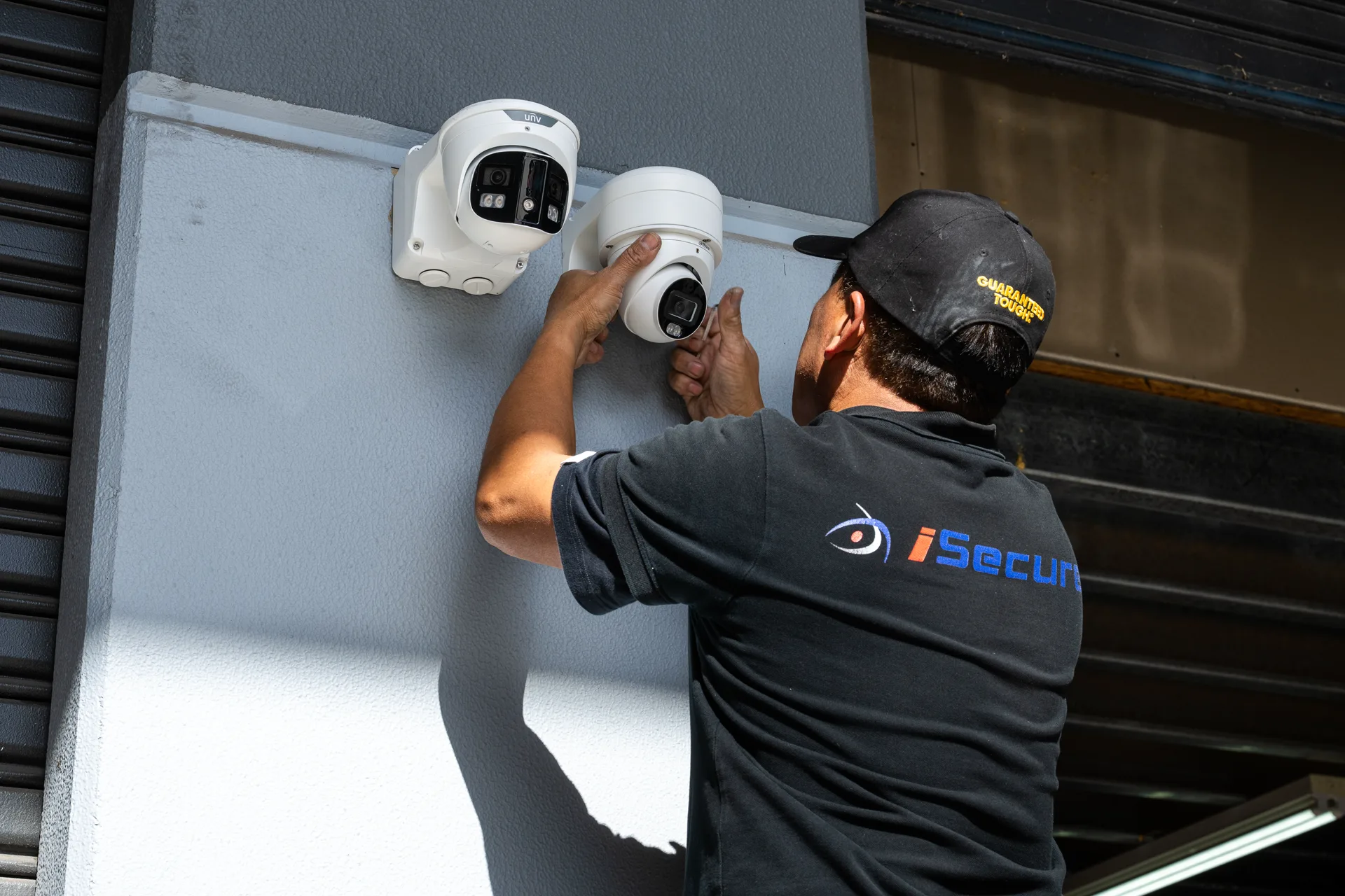 An iSecure technician installing cameras on a commercial wall